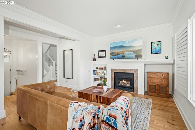 living room featuring visible vents, a tiled fireplace, stairway, ornamental molding, and light wood-style flooring