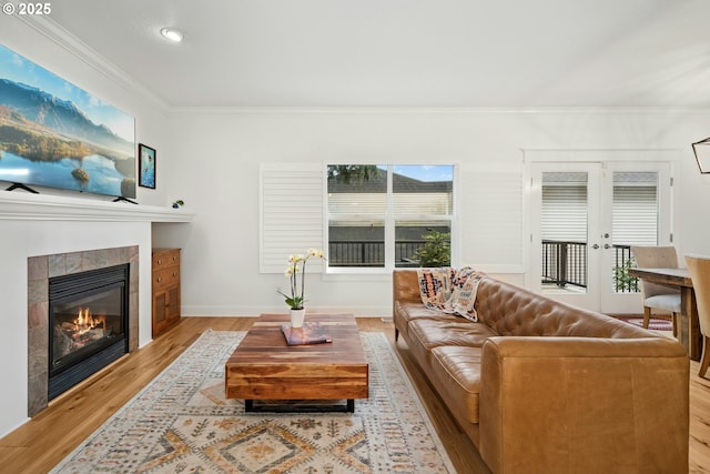 living area featuring a healthy amount of sunlight, wood finished floors, crown molding, and a tiled fireplace