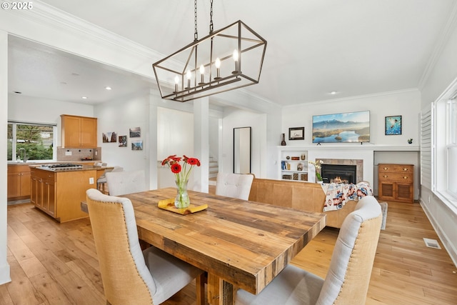 dining space featuring recessed lighting, light wood-type flooring, ornamental molding, and a tiled fireplace