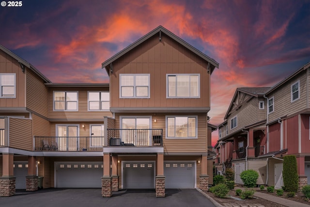 multi unit property featuring a garage, board and batten siding, driveway, and stone siding