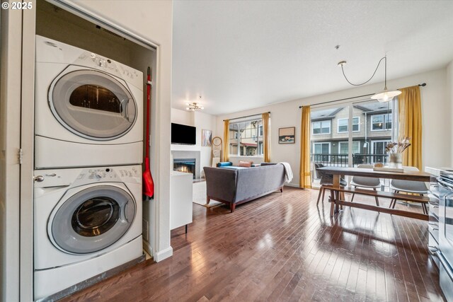 clothes washing area featuring wood-type flooring, stacked washer / drying machine, a lit fireplace, and laundry area