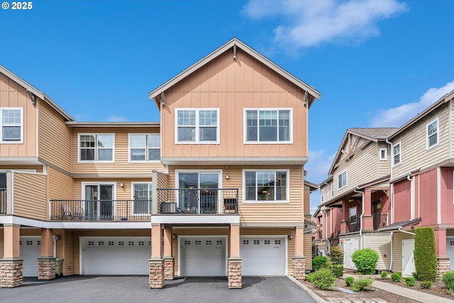 townhome / multi-family property featuring board and batten siding, driveway, stone siding, and a garage