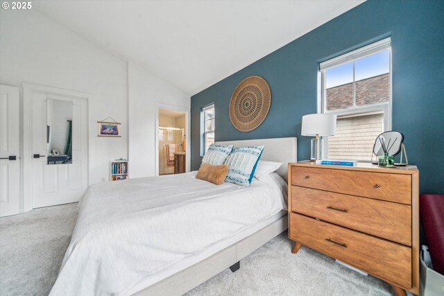 bedroom with light colored carpet, lofted ceiling, and ensuite bath