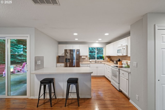 kitchen featuring visible vents, backsplash, white appliances, a peninsula, and white cabinets