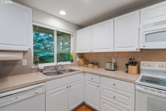 kitchen with backsplash, white appliances, white cabinets, and a sink