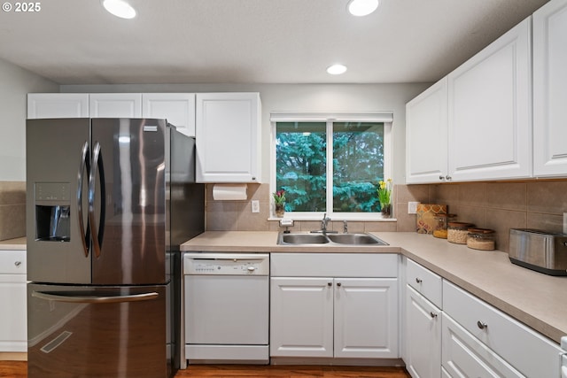 kitchen featuring decorative backsplash, stainless steel refrigerator with ice dispenser, white dishwasher, white cabinetry, and a sink