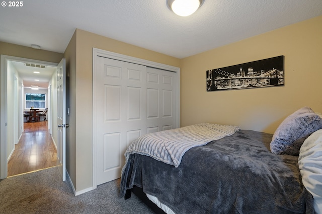 carpeted bedroom featuring a closet, visible vents, a textured ceiling, and baseboards