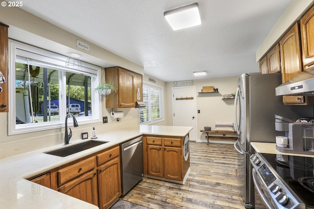 kitchen featuring sink, appliances with stainless steel finishes, wood-type flooring, a textured ceiling, and kitchen peninsula