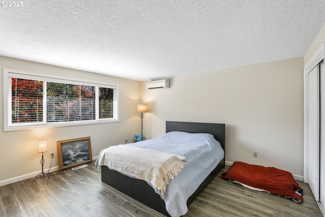 bedroom with hardwood / wood-style flooring, a wall mounted AC, a textured ceiling, and a closet