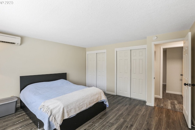 bedroom with multiple closets, a wall mounted air conditioner, dark wood-type flooring, and a textured ceiling