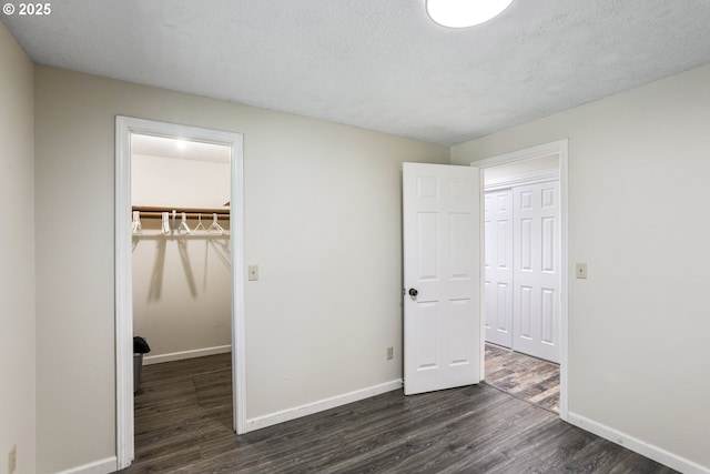 unfurnished bedroom featuring a walk in closet, dark hardwood / wood-style flooring, a closet, and a textured ceiling