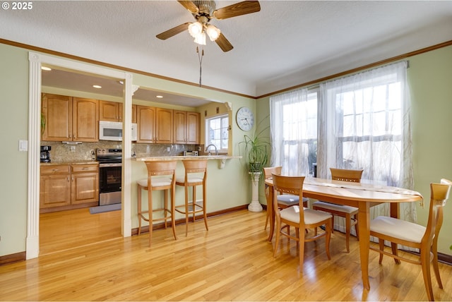 dining room with light wood-type flooring, ceiling fan, baseboards, and a textured ceiling