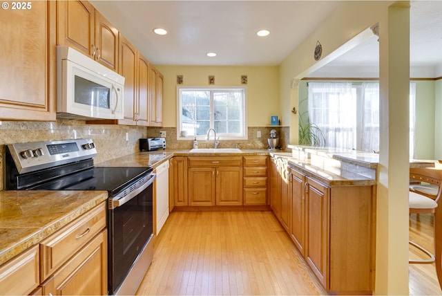 kitchen featuring white appliances, tasteful backsplash, a peninsula, light wood-type flooring, and a sink