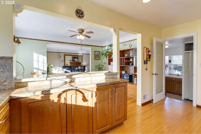 kitchen with brown cabinets, visible vents, light wood-style floors, ceiling fan, and a peninsula