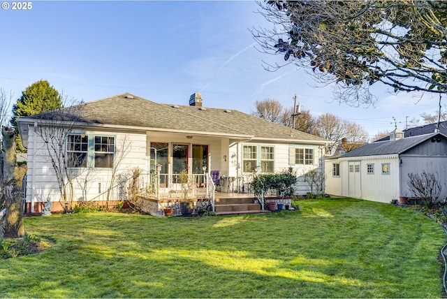 rear view of house with a shingled roof, an outbuilding, a lawn, and a chimney