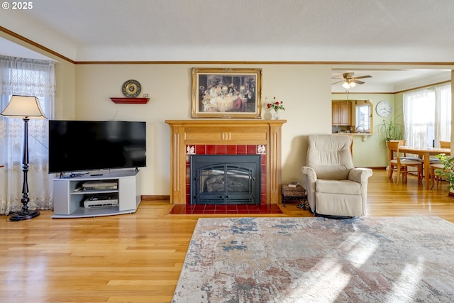 living room with baseboards, a tile fireplace, wood finished floors, crown molding, and a textured ceiling