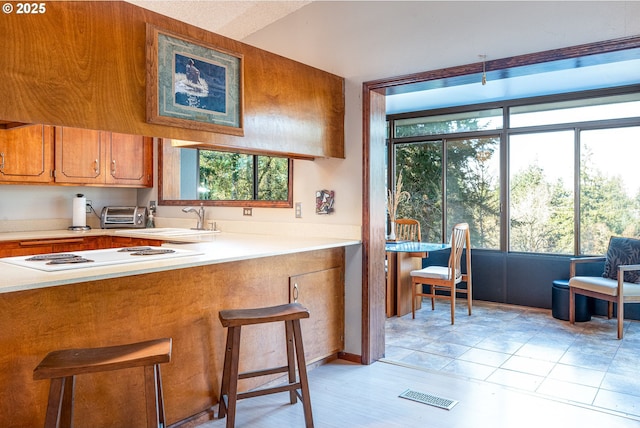 kitchen with white cooktop, a breakfast bar area, sink, and light tile patterned flooring