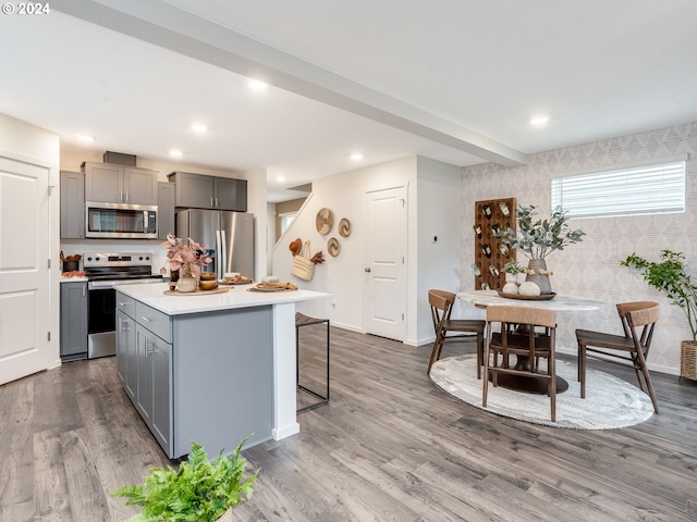 kitchen with appliances with stainless steel finishes, a center island, wood-type flooring, a breakfast bar, and gray cabinetry