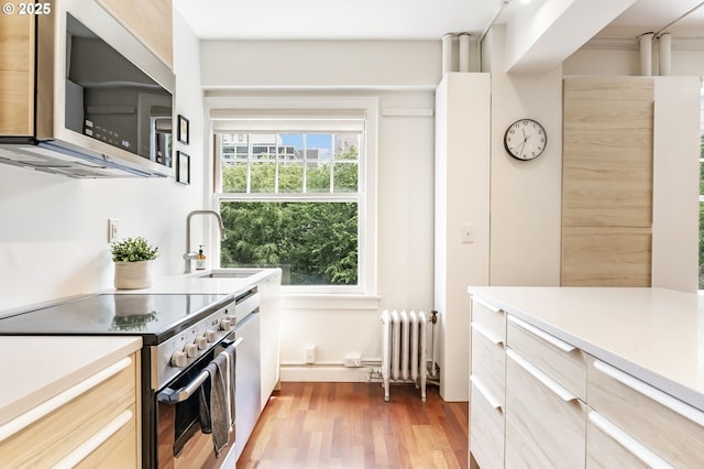 1005 SW Park Ave Unit 607, Portland, OR 97205 - kitchen with appliances with stainless steel finishes, radiator heating unit, wood finished floors, light countertops, and a sink