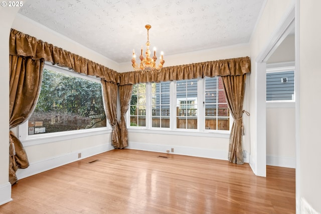 unfurnished dining area featuring a chandelier, wood-type flooring, a textured ceiling, and crown molding