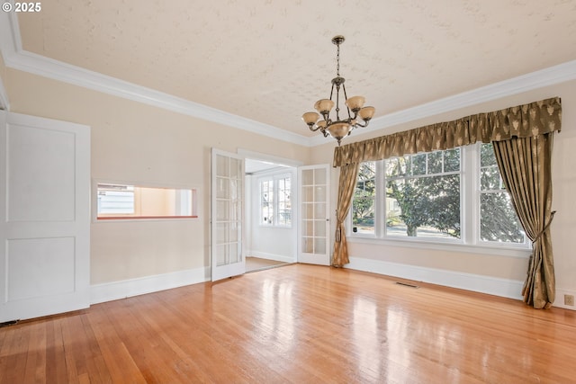 empty room featuring hardwood / wood-style flooring, a notable chandelier, crown molding, and french doors