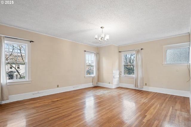 spare room featuring a textured ceiling, light wood-type flooring, an inviting chandelier, and plenty of natural light