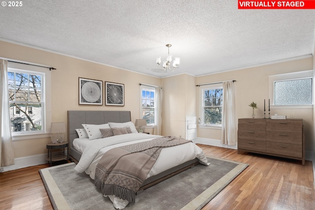 bedroom featuring a chandelier, a textured ceiling, light hardwood / wood-style floors, and crown molding