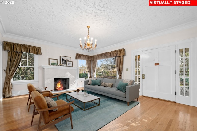 living room with ornamental molding, light hardwood / wood-style floors, a textured ceiling, a fireplace, and a chandelier