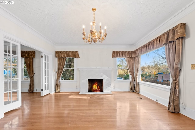 unfurnished living room featuring plenty of natural light, a premium fireplace, ornamental molding, and a chandelier