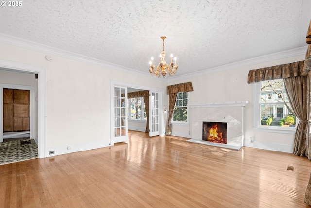 unfurnished living room with light hardwood / wood-style floors, ornamental molding, a fireplace, and an inviting chandelier