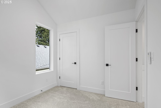unfurnished bedroom with light colored carpet, vaulted ceiling, and baseboards