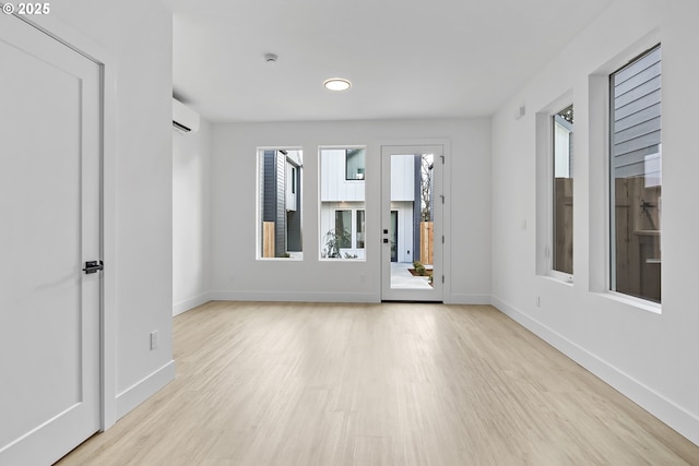unfurnished room with a wall mounted AC, baseboards, and wood finished floors