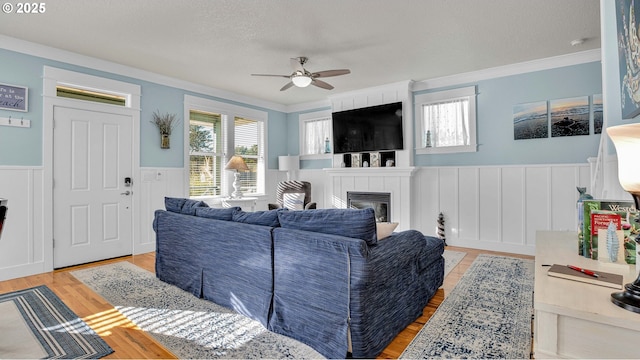 2781 SW Coast Ave, Lincoln City, OR 97367 - living room featuring a ceiling fan, a wainscoted wall, crown molding, light wood-style flooring, and a fireplace