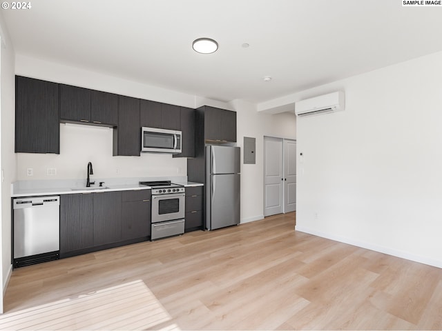 kitchen with appliances with stainless steel finishes, a wall unit AC, sink, light hardwood / wood-style flooring, and electric panel