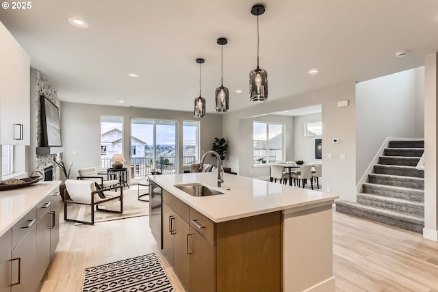 kitchen featuring a center island with sink, open floor plan, hanging light fixtures, light countertops, and a sink