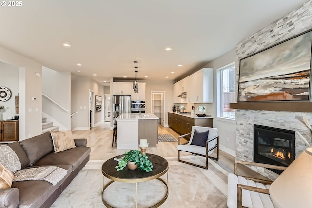 living area featuring recessed lighting, a fireplace, light wood finished floors, and stairs