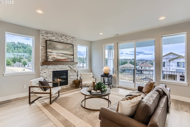 living room with light wood finished floors, recessed lighting, visible vents, a stone fireplace, and baseboards