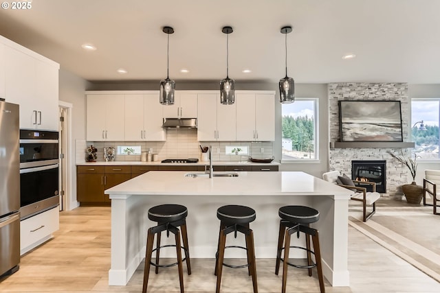 kitchen with a kitchen island with sink, light countertops, a sink, and hanging light fixtures