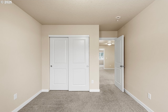 unfurnished bedroom with light colored carpet, a closet, and a textured ceiling