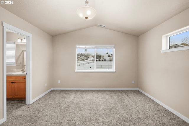 unfurnished bedroom with lofted ceiling, sink, light colored carpet, and ensuite bath