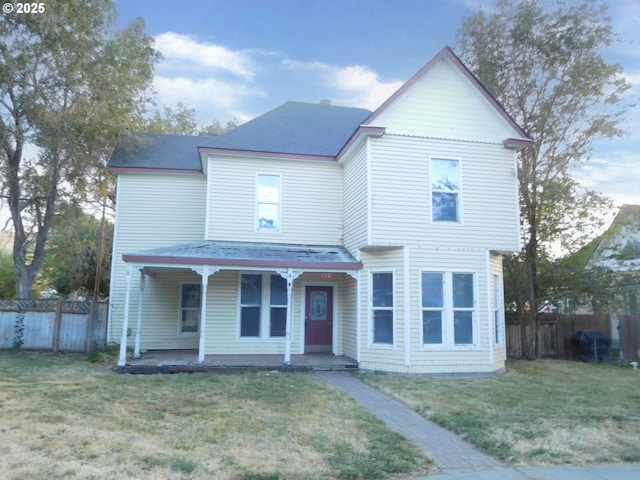 victorian-style house featuring covered porch, a front lawn, and fence