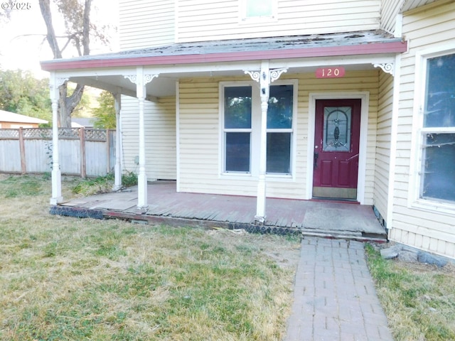 doorway to property featuring covered porch, fence, and a lawn