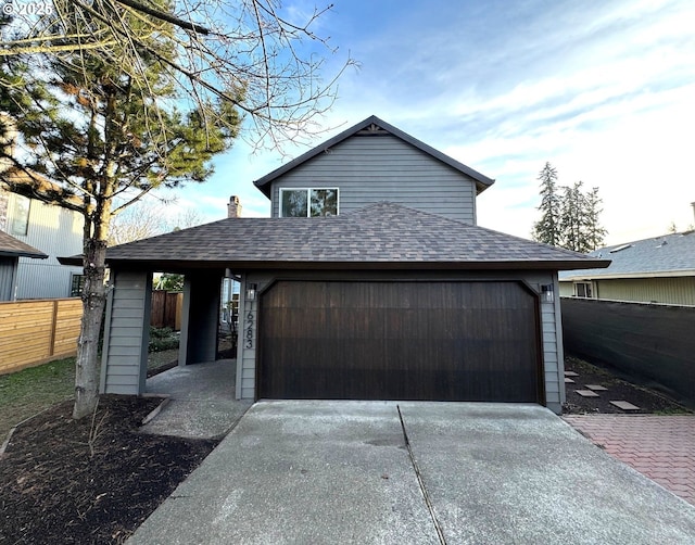 view of front facade with a garage, concrete driveway, a shingled roof, and fence