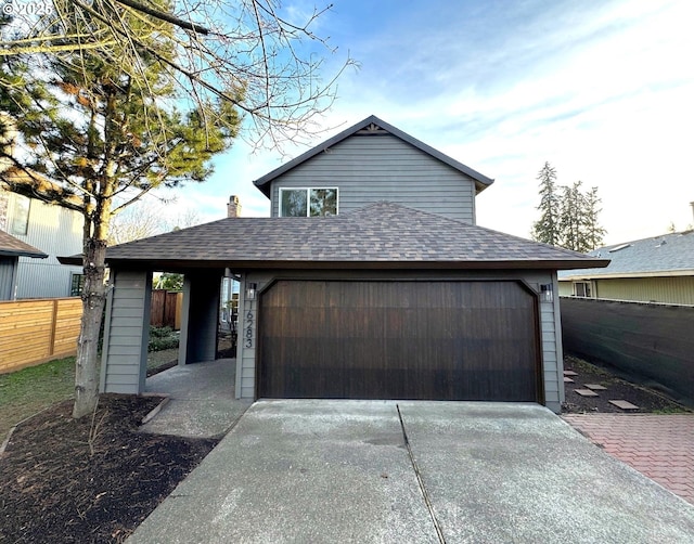 view of front of home featuring driveway, a shingled roof, an attached garage, and fence