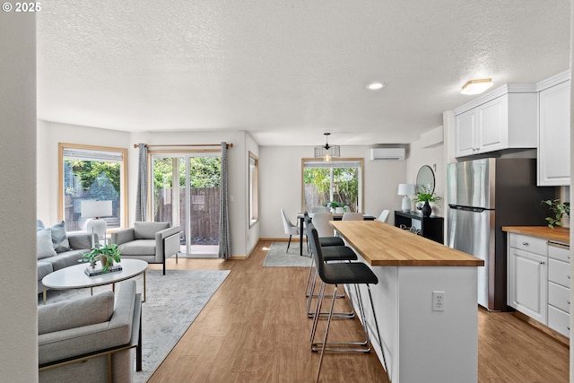 6309 NE 45th Ave, Portland, OR 97218 - kitchen with butcher block countertops, freestanding refrigerator, a wall unit AC, white cabinets, and a kitchen bar