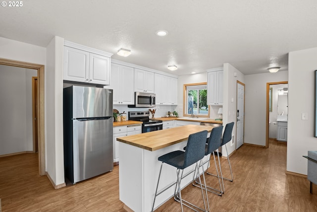 6309 NE 45th Ave, Portland, OR 97218 - kitchen with appliances with stainless steel finishes, butcher block counters, a breakfast bar, white cabinetry, and light wood-style floors