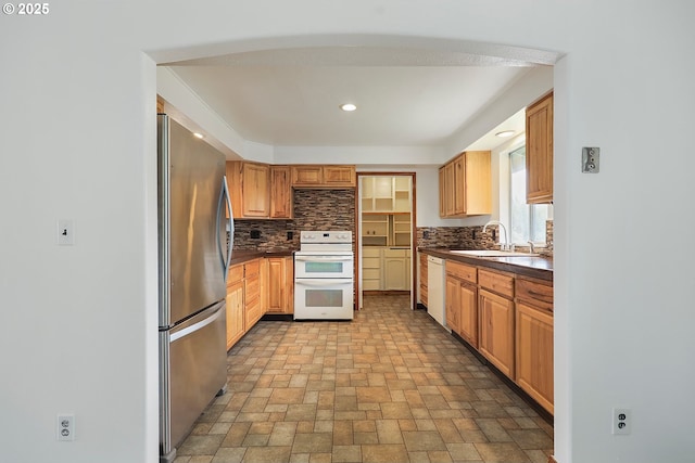 kitchen featuring a sink, decorative backsplash, white appliances, and dark countertops