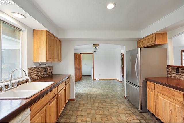 kitchen with dark countertops, decorative backsplash, freestanding refrigerator, white dishwasher, and a sink