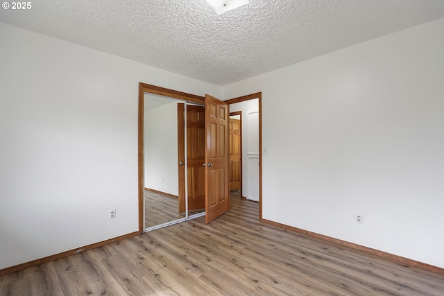 unfurnished bedroom featuring a closet, baseboards, a textured ceiling, and light wood-style flooring