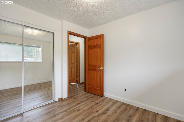 unfurnished bedroom featuring a closet, baseboards, a textured ceiling, and wood finished floors